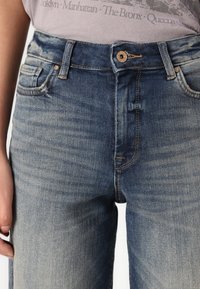Høy midje blå denimjeans med en falmet finish, med klassisk fem-lommers design, synlig søm, og en frontknapp lukking.