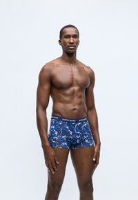 Sötétkék boxeralsó, sokszínű absztrakt mintával. Rugalmas anyagból készült, márkázott derékpánttal és combközép hosszúsággal.