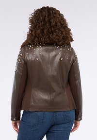 Giubbotto in pelle marrone con dettagli decorativi alle spalle che presentano diverse gemme; texture liscia, design aderente e chiusura a scatto sui polsini.