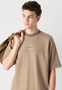 Brown cotton T-shirt with a crew neck, short sleeves, and tonal logo detail. The fabric has a smooth texture and relaxed fit.