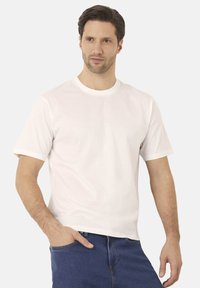 Bílý bavlněný tričko s krátkými rukávy, kulatým výstřihem a volným střihem. Nošeno s modrými džínami, má jednoduchý design bez vzorů.