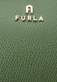 Zelená strukturovaná kůže s embosovaným vzorem; ve středu je umístěno metalické zlaté logo "FURLA". Hladký povrch s jemným leskem.