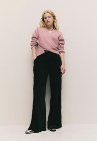 Lys rosa fuzzy striktrøje med v-hals, parret med brede sorte bukser og metalliske spidse sko.