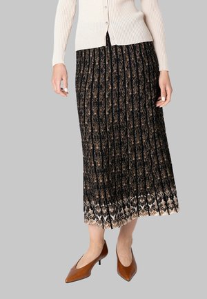 Donna che indossa una gonna midi plissettata con fantasia nera e marrone, cardigan beige a coste con bottoni e décolleté marroni con punta appuntita e tacco basso.