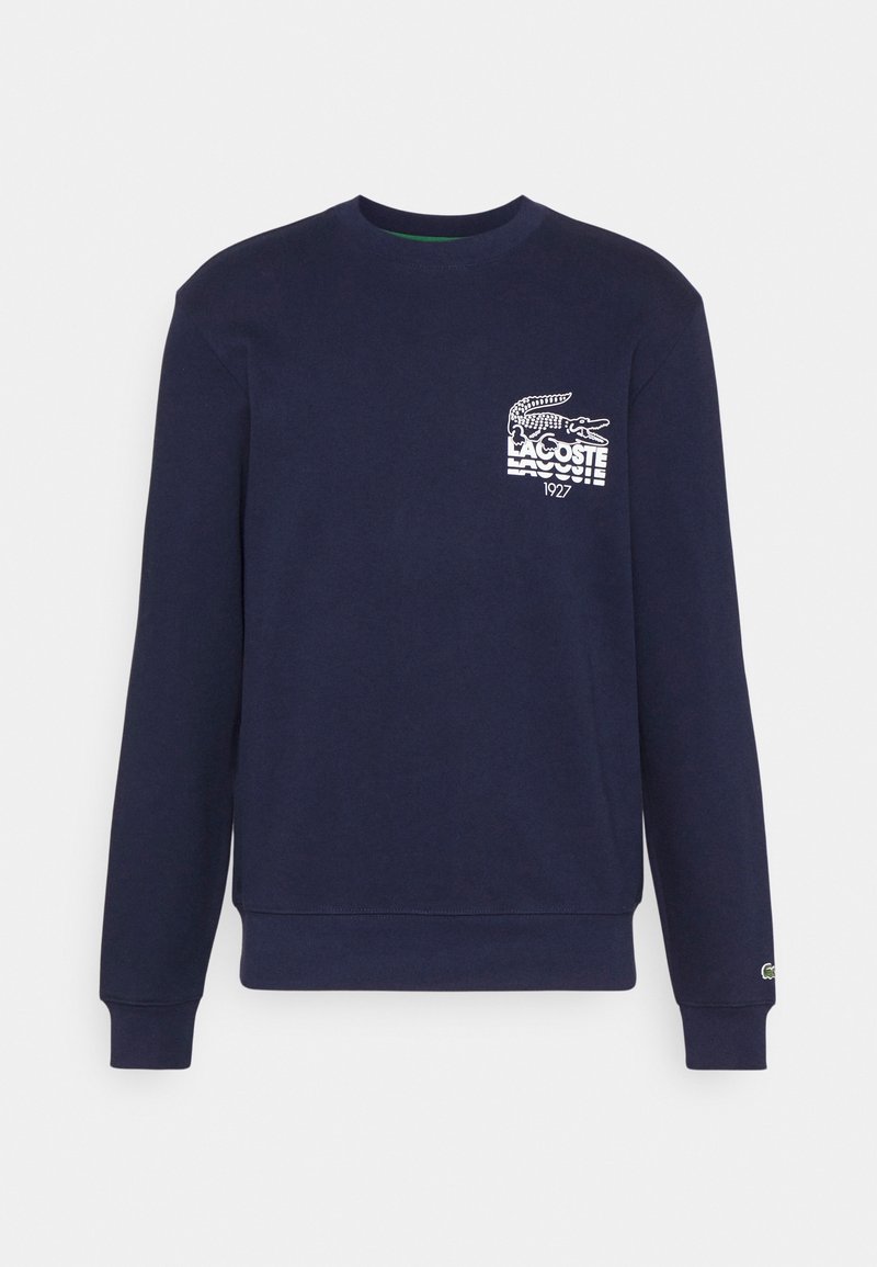 Felpa blu navy con maniche lunghe, colletto rotondo, caratterizzata da un logo Lacoste bianco e un grafico di coccodrillo sul lato sinistro del petto.