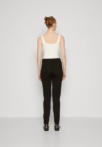Črne krojene hlače s slim fit krojem, diskretnimi zadnjimi žepi in gladko teksturo, v kombinaciji z oprijetim belim topom.
