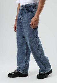 Blauwe wijde denimjeans met een vervaagde afwerking, ontwerp met vijf zakken en een hoge taille. Gecombineerd met zwarte chunky schoenen met metalen ogen.