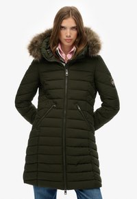 Abrigo acolchado color verde oliva con capucha forrada de piel, cierre frontal con cremallera y bolsillos laterales. Patrón texturizado con secciones acolchadas.