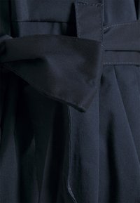 Navy stof jurk met een geplooid ontwerp, voorzien van een gestrikten strikaccent op de taille en een gladde textuur. Zomen zijn zichtbaar langs de randen.