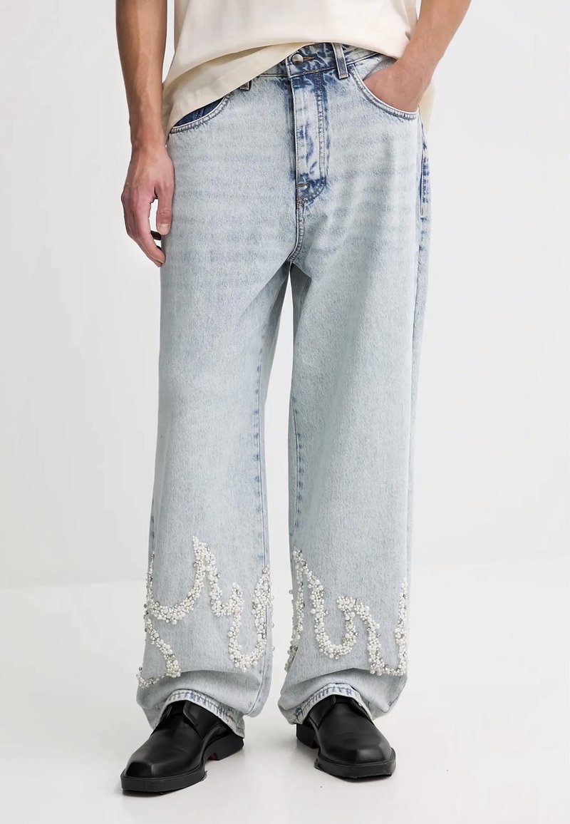 Jeans in denim azzurro chiaro con gambe larghe, caratterizzati da intricate decorazioni in perline bianche lungo i orli. Design minimalista con tasche frontali.