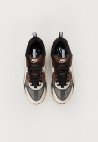 Tenisky so hnedým a čiernym zvrškom s béžovými akcentmi, sieťovinou, mriežkovým vzorom a čiernymi šnúrkami. Logo Nike na jazyku.