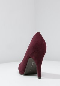 Burgundyröd högklackad sko med spetsig tå, tillverkad av ett mockaliknande material, med en slank silhuett och en tunn, avsmalnande klack.