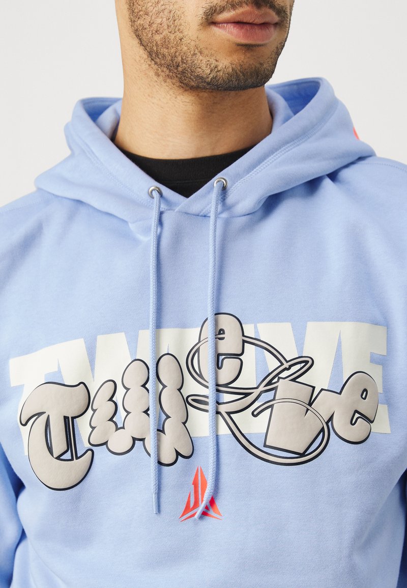 Sudadera azul claro con un gran diseño gráfico en letras burbuja y acentos, cordones, y un pequeño logo rojo en el dobladillo.