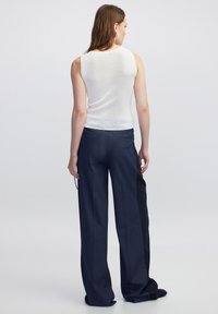 Witte mouwloze top gecombineerd met donkerblauwe wijde broek met een streepdetail aan één kant. Slim fit met een textuurafwerking.