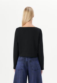 Svart kortärmad topp med fyrkantig halsringning, kombinerad med blå högmidjade vida jeans med bakfickor och ljus tvätt.