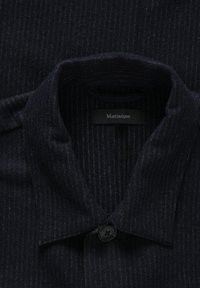 Col de chemise à fines rayures foncé avec un bouton noir et une étiquette indiquant "Matinique" à l'intérieur de l'encolure.