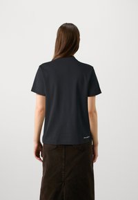 Juodas medvilnės marškinėlis su klasikiniu kirpimu, trumpomis rankovėmis ir apvalia iškirpte. Atgaliniame siūle subtiliai pašalinta ženklas.