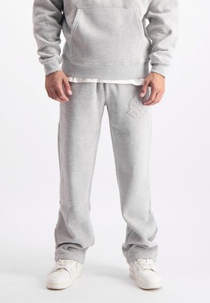 Grijze hoodie met een kangoeroezak en joggingbroek met een reliëflogo, beide gemaakt van zachte, textuurstof, gecombineerd met witte sneakers.