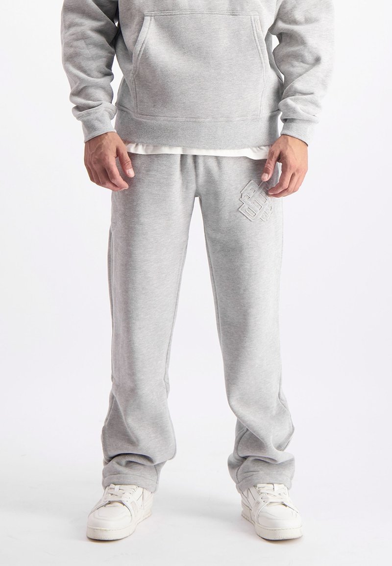Grijze hoodie met een kangoeroezak en joggingbroek met een reliëflogo, beide gemaakt van zachte, textuurstof, gecombineerd met witte sneakers.