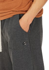 Mörkgrå träningsoverallsbyxor i bomullsblandning, med en sidoficka och en liten svart logotypdetalj. Resårmidjan har en dragsko.