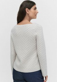 Haut à manches longues gris clair avec un motif en chevrons subtil. Encolure arrondie et texture lisse, associé à un jean bleu foncé.
