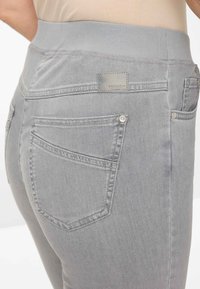 Grijze denim jeans met een elastische tailleband, voorzien van achterzakken en een merklabel. De stof heeft een gladde textuur en een getailleerd silhouet.