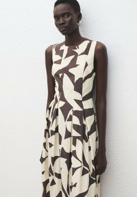 Vestido sin mangas con corpiño ajustado, hecho de una tela ligera con un patrón abstracto de hojas marrones sobre un fondo crema.