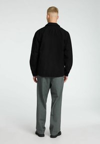 Giacca nera dal taglio rilassato, con colletto e maniche lunghe. Abbinata a pantaloni grigi su misura e calzature nere.