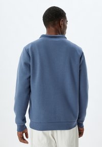 Herrenpullover aus weichem blauem Stoff mit gerippten Bündchen und Saum. Verfügt über einen klassischen Kragen und ein einfaches Design ohne sichtbare Logos.