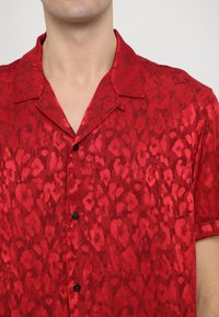 Rood shirt met korte mouwen in een zachte, satijnachtige stof, voorzien van een subtiele luipaardprint, met een camp collar en zwarte knopen.