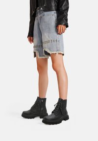 Stivaletti neri alla caviglia con finitura texture, lacci davanti e zip laterale. Abbinati a pantaloncini di jeans sfilacciati con borchie metalliche.