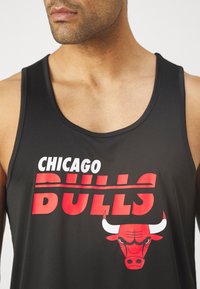 Fekete trikó, amelyen a "CHICAGO BULLS" felirat fehér és piros színben, piros bika grafikával és kontrasztos díszítésekkel szerepel. Sima textúra, ujjatlan kialakítás.
