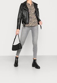 Veste de motard en cuir noir, blouse à fleurs, jean skinny gris, bottines à talons noires, et un petit sac à main noir avec une bandoulière.