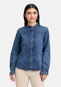 Jeansowa kurtka w ciemnoniebieskim kolorze, z falbaniastym kołnierzem, zapięciem na guziki i teksturowanym materiałem. Długie rękawy z falbaniastymi brzegami.