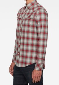 Rode en grijze geruite flanellen shirt met lange mouwen, knoopsluiting, twee borstzakken en een afgeronde zoom. Het materiaal lijkt zacht met een gestructureerde weving.