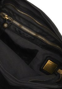 Interno di una borsa in pelle nera con molteplici scomparti; presenta accessori in oro, chiusure a zip e una fodera in tessuto con branding impresso.