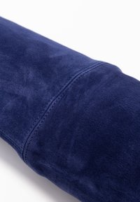 Marineblauer Wildlederstoff, glatte Textur, zeigt eine Nahtdetail. Abgerundete Form mit einem subtilen Glanz. Keine sichtbaren Hardware-Elemente oder Muster.