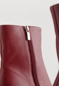 Bordeauxrote Leder-Stiefeletten mit seitlichem Reißverschluss und glatter Textur, mit minimalen Nähten und schlanker Silhouette.