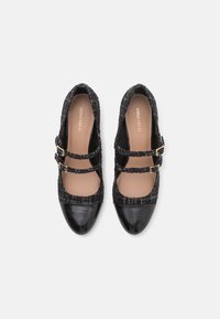 Svarta Mary Jane-skor med en tweed-överdel, två remmar med guldspännen och en rund tå. Slät svart lackläderkappa.