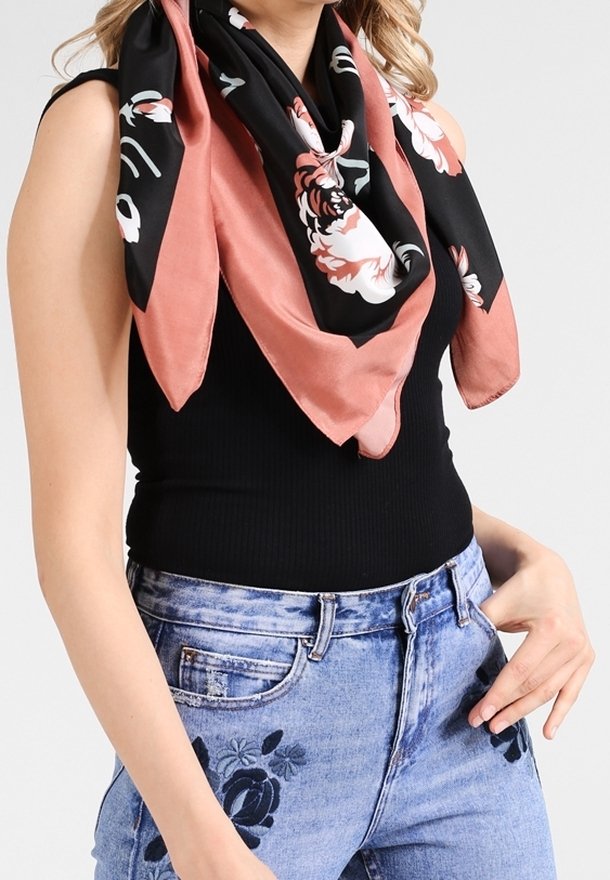 Femme portant un haut noir sans manches, un jean bleu brodé de fleurs et une écharpe fleurie noire et rose autour du cou.