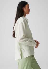 Blusa a righe verde chiaro con colletto, maniche lunghe e dettaglio con nodo sul lato. Tessuto testurizzato con una vestibilità comoda.