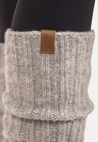 Calentador de piernas de lana gris claro tejido con costillas verticales y una pequeña etiqueta de cuero marrón con la inscripción "VIVI SENCE".