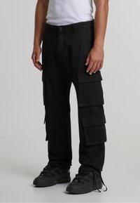 Pantaloni cargo negri cu multiple buzunare laterale, croială lejeră și material rezistent. Asortați cu adidași negri și un maiou alb.