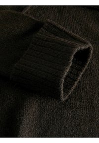 Tessuto di maglione lavorato a maglia di colore marrone scuro che mostra un primo piano di un polsino a coste e un corpo texturizzato, evidenziando il materiale morbido e peloso.