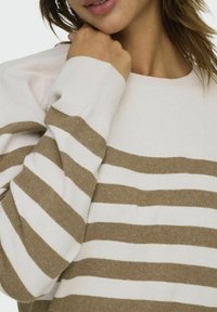 Pull rayé en crème et marron clair, avec des poignets côtelés et un design à col rond. Texture douce avec des rayures horizontales contrastantes.