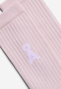 Hellrosa, gerippte Socken mit einem weißen Logo. Das Material wirkt weich mit einer strukturierten Oberfläche, die das Design und die Markendetails hervorhebt.