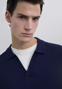 Suéter de lana azul marino de punto con escote en V, cuello corto, usado sobre una camiseta de cuello redondo blanca, textura suave y líneas limpias.