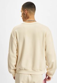 Beige pulóver kerek nyakkal, bordás mandzsettával és aljjal. Sima textúra, laza fazon, sima hátoldallal, díszítések nélkül.