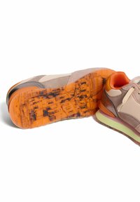 Sneaker con tomaia in suede beige, accenti grigi, un intersuola arancione e una suola traslucida arancione texturizzata con dettagli a motivo.