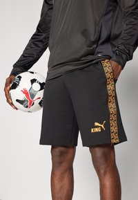 Czarne spodenki sportowe z pomarańczowym logo "KING" i wzorzystymi detalami po bokach. W zestawie czarna koszulka z długim rękawem oraz biały piłka nożna.